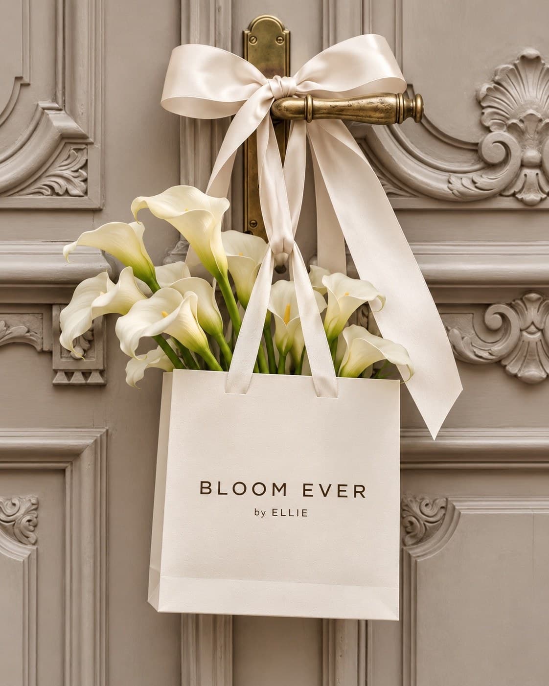 A white bag filled with calla lilies, tied with an ivory satin bow, hanging on a carved wooden door.